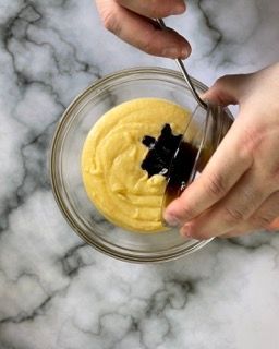 Una persona sta mescolando una salsa gialla in una ciotola di vetro con un cucchiaio.