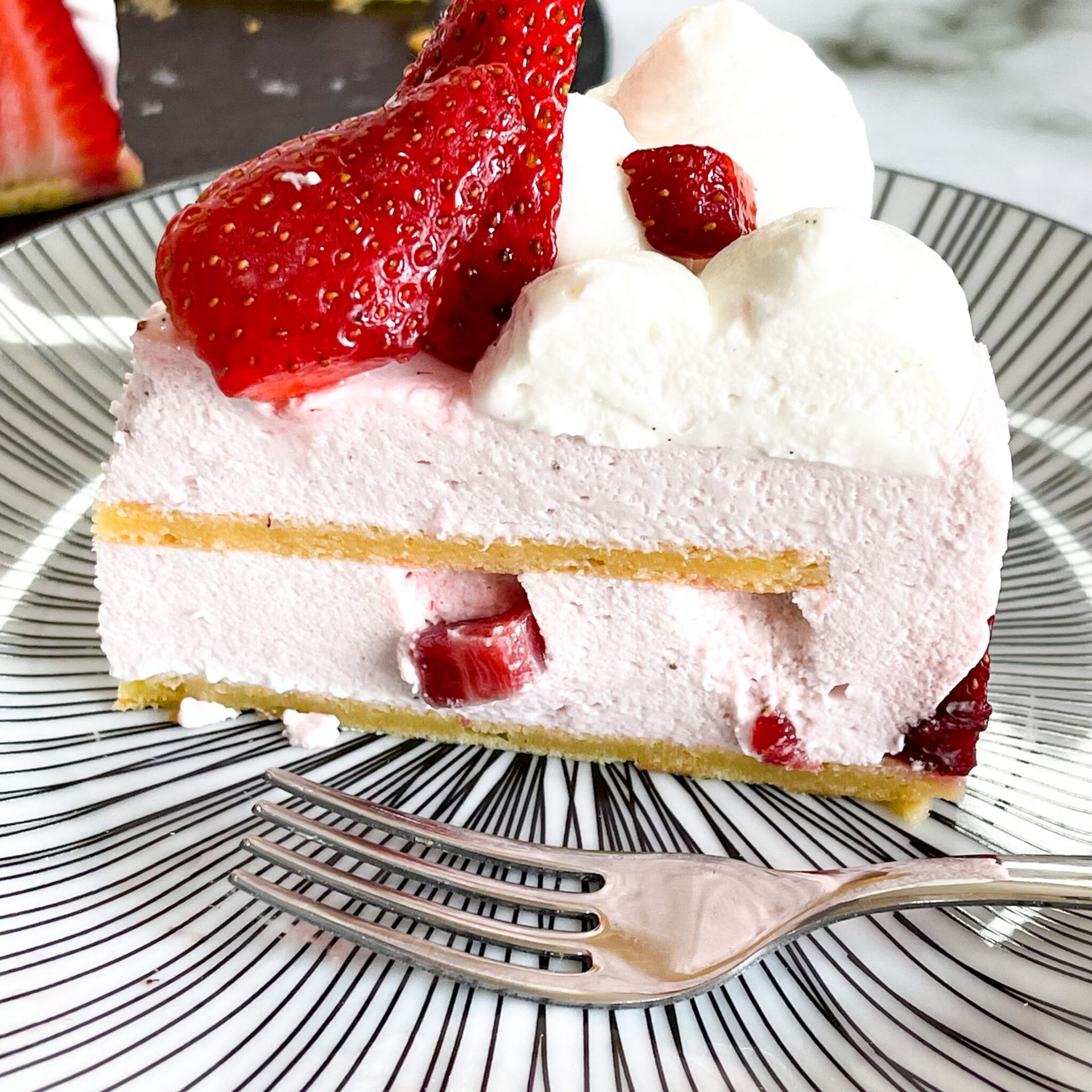 Una fetta di torta con fragole e panna montata su un piatto con una forchetta.