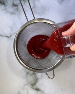 Una persona sta versando del liquido rosso in un colino.