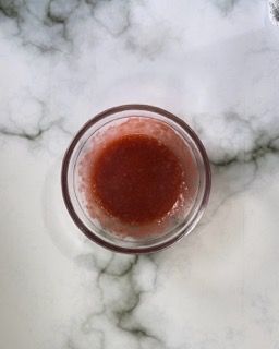 Un piccolo bicchiere pieno di liquido rosso è appoggiato su un tavolo.