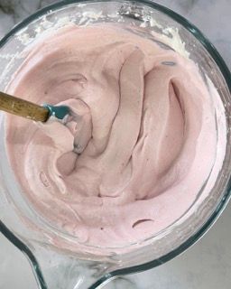 Una ciotola di vetro piena di glassa rosa con una spatola dentro.
