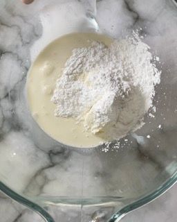 Una persona sta versando la farina in una ciotola piena di liquido.