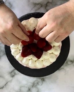 Una persona sta decorando una torta con fragole e panna montata