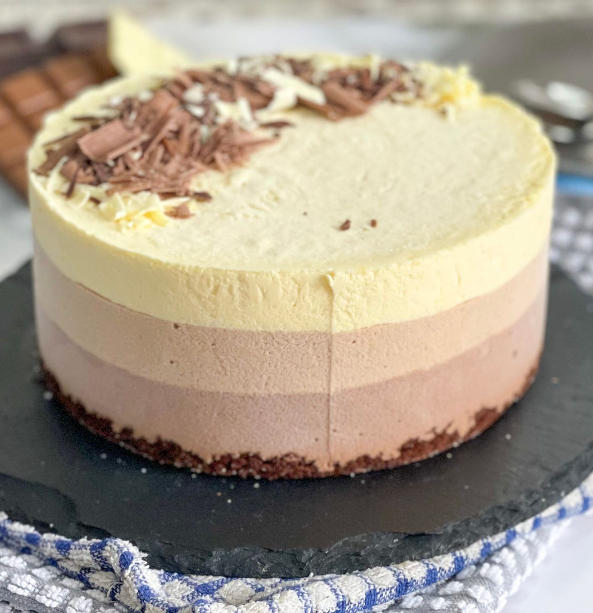 Una torta a tre strati con scaglie di cioccolato sopra è appoggiata su un piatto nero.