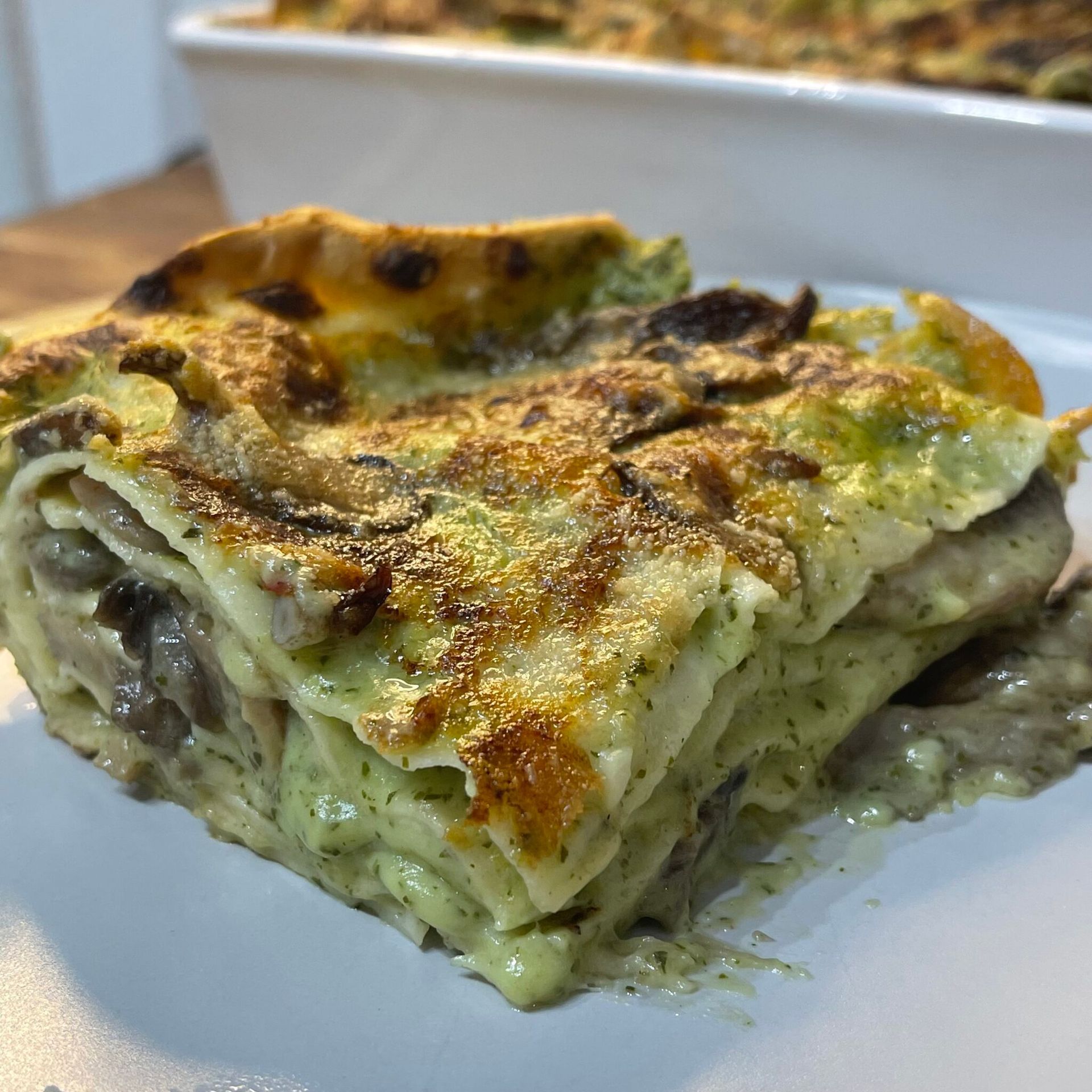 Una fetta di lasagna è su un piatto bianco.