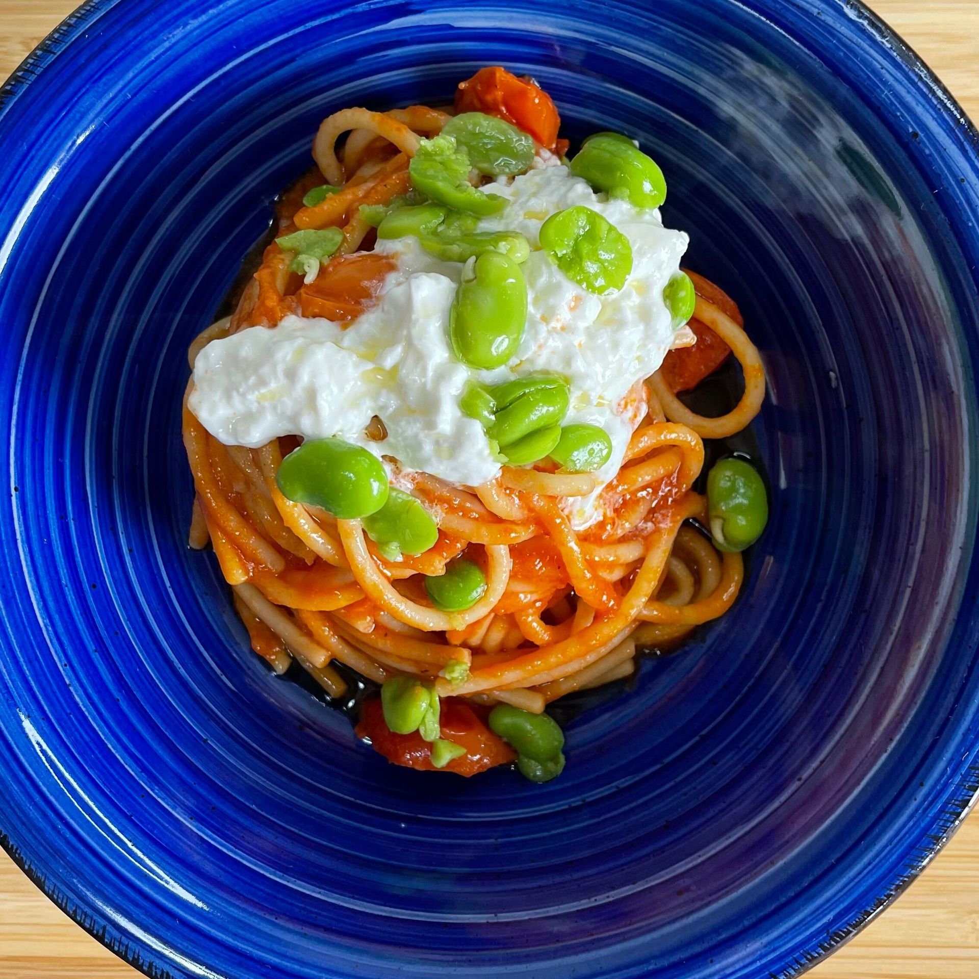 Un piatto blu con sopra spaghetti e fagioli su un tavolo di legno.