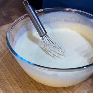 Una ciotola di vetro piena di liquido bianco e una frusta al suo interno