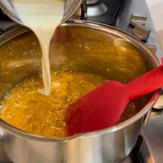 Una persona che versa del liquido in una pentola con una spatola rossa