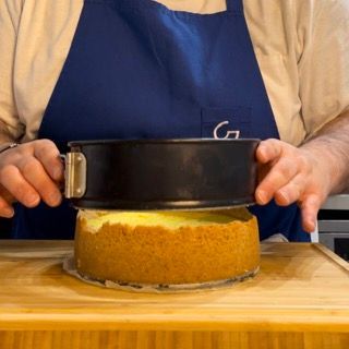 Una persona con un grembiule tiene una tortiera sopra una torta