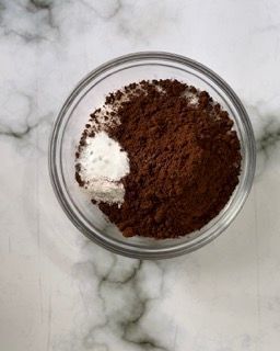 Una ciotola di vetro piena di cacao in polvere e bicarbonato di sodio su un tavolo.