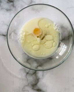 Una ciotola di vetro piena di un liquido giallo e un uovo.