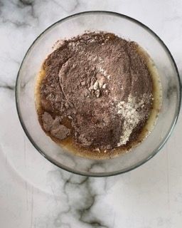 Una ciotola di vetro piena di cioccolato in polvere e liquido su un tavolo.