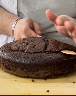 Una persona sta tagliando una torta al cioccolato su un tagliere di legno