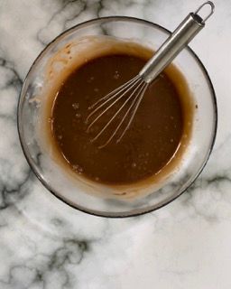 Una ciotola di liquido marrone con una frusta dentro