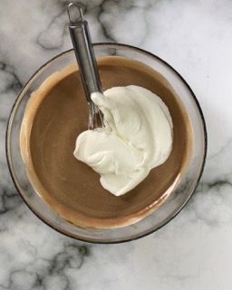 Una ciotola di budino al cioccolato con panna montata e un cucchiaio dentro