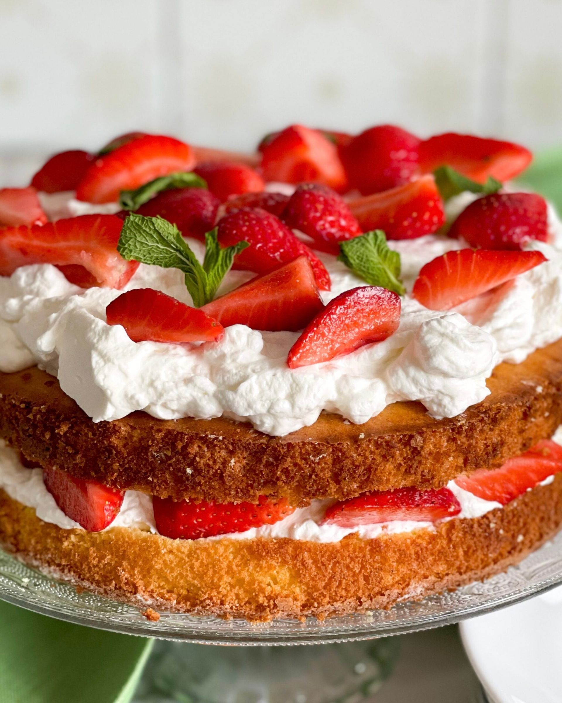 Una torta con fragole e panna montata su un piatto di vetro.