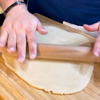 Una persona sta stendendo un pezzo di pasta con un mattarello