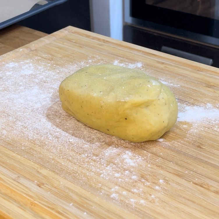 Una palla di pasta è appoggiata su un tagliere di legno ricoperto di farina.