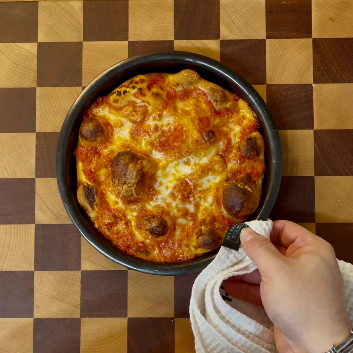 Una persona tiene un asciugamano sopra una pizza su un tavolo a scacchi