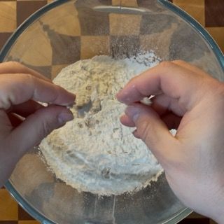 Una persona sta mescolando la farina in una ciotola di vetro