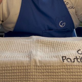 Una persona che indossa un grembiule blu tiene in mano un asciugamano con la scritta pasticceria