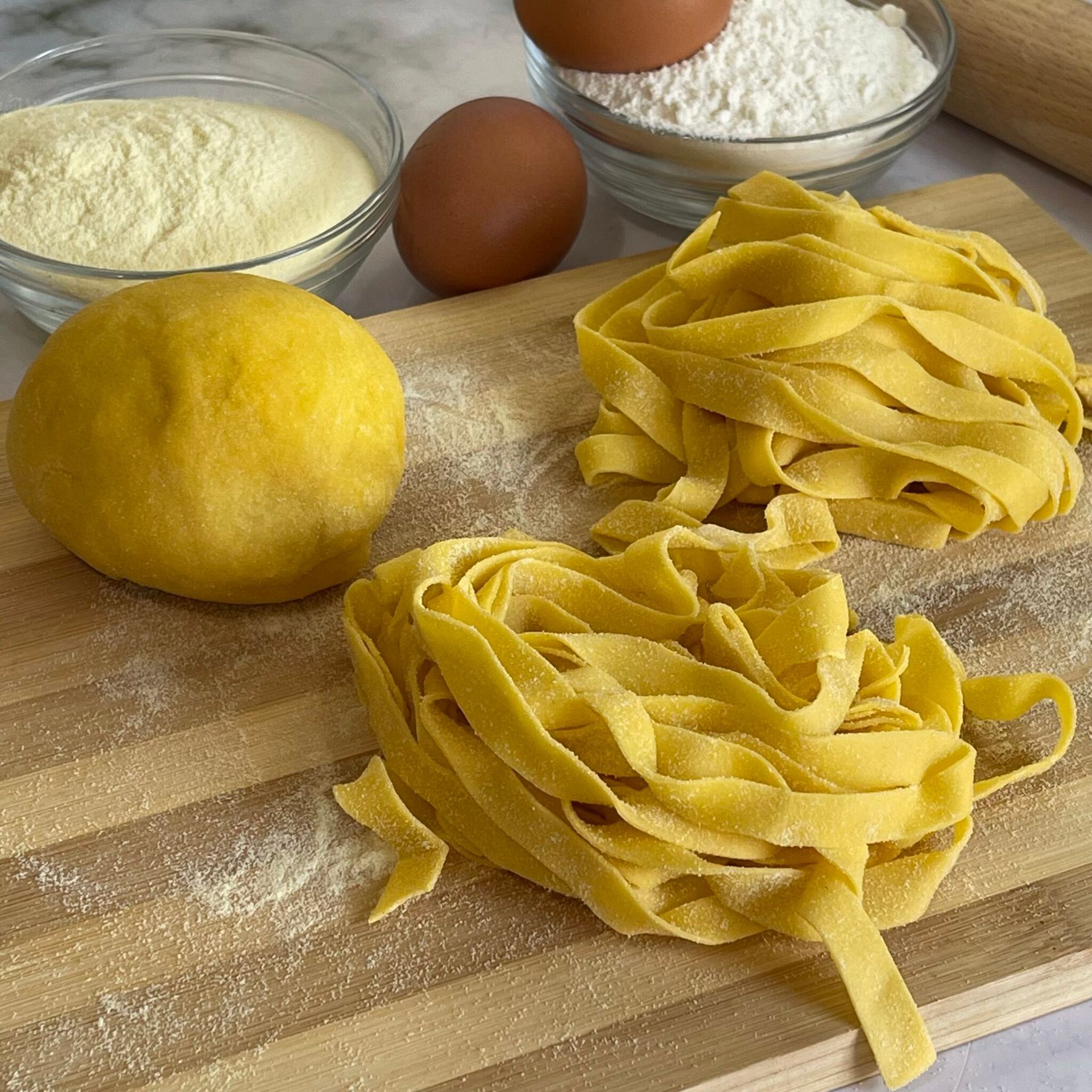 Un tagliere di legno con sopra tagliatelle e uova