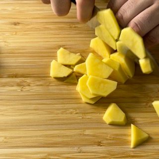 Una persona sta tagliando le patate su un tagliere di legno