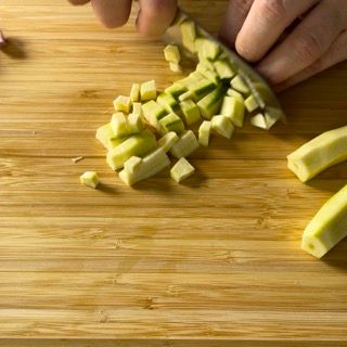 Una persona sta tagliando le verdure su un tagliere di legno.