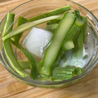Una ciotola di vetro piena di verdure verdi e cubetti di ghiaccio su un tavolo di legno.