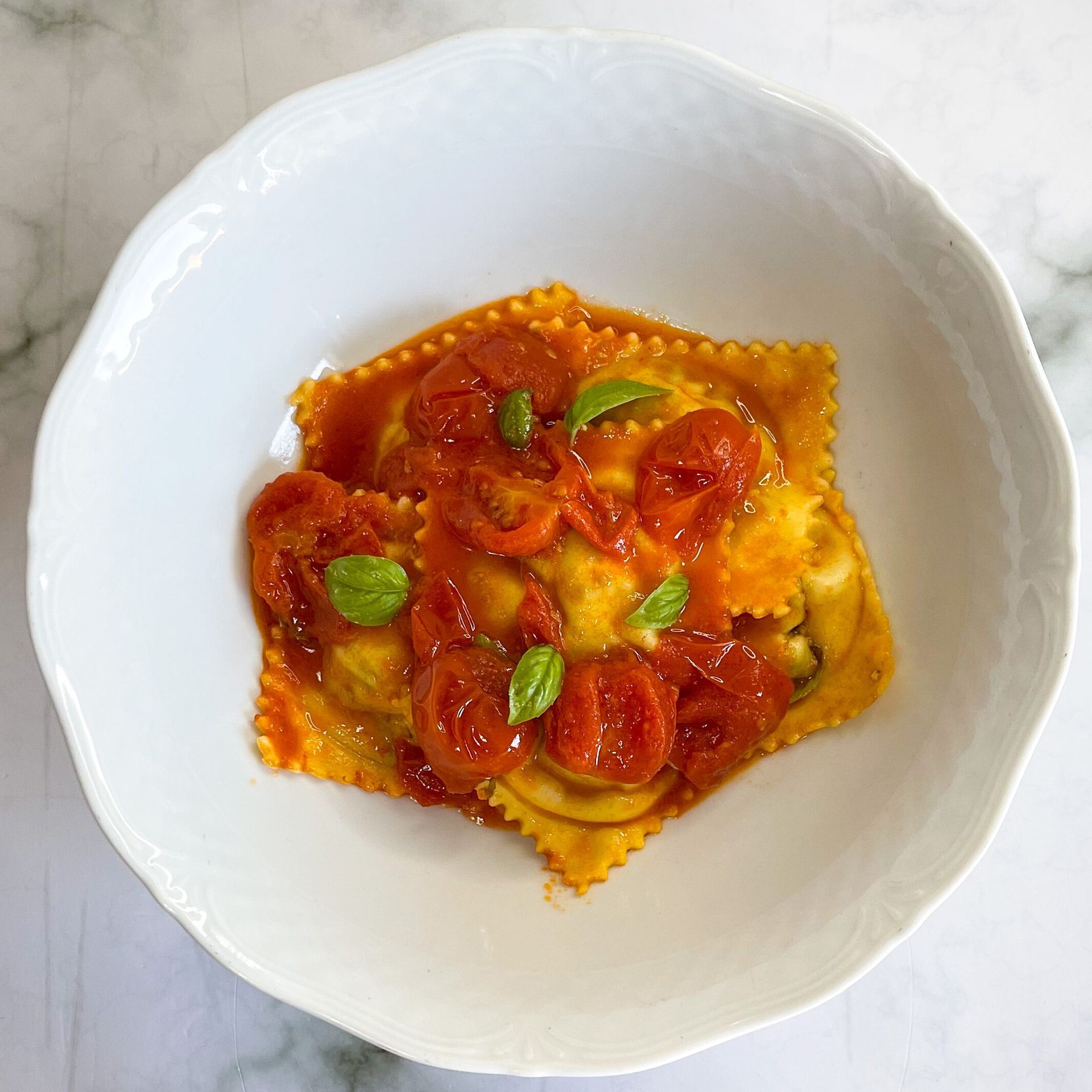 Una ciotola bianca piena di ravioli e salsa di pomodoro su un tavolo.