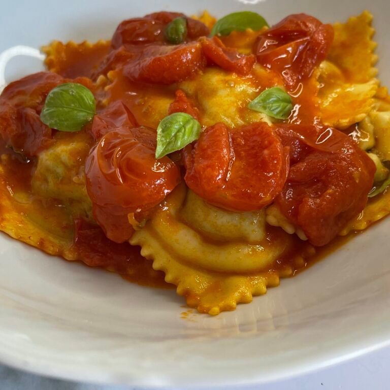 Un piatto bianco condito con ravioli e salsa di pomodoro