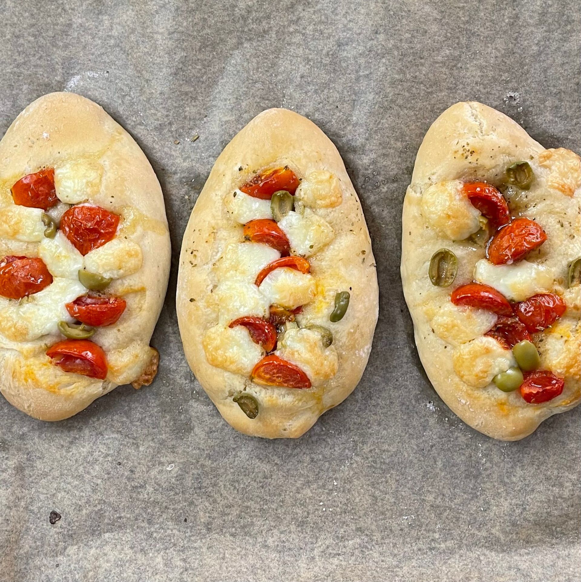 Tre pizze con pomodori e olive sono appoggiate su un tavolo.