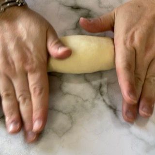 Una persona sta stendendo un pezzo di pasta con un mattarello.