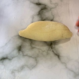 Una persona tiene in mano un pezzo di pasta su una superficie di marmo.