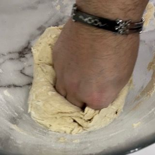 Una persona impasta l'impasto in una ciotola con il pugno.