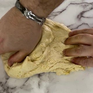 Una persona sta impastando un pezzo di pasta su una superficie di marmo
