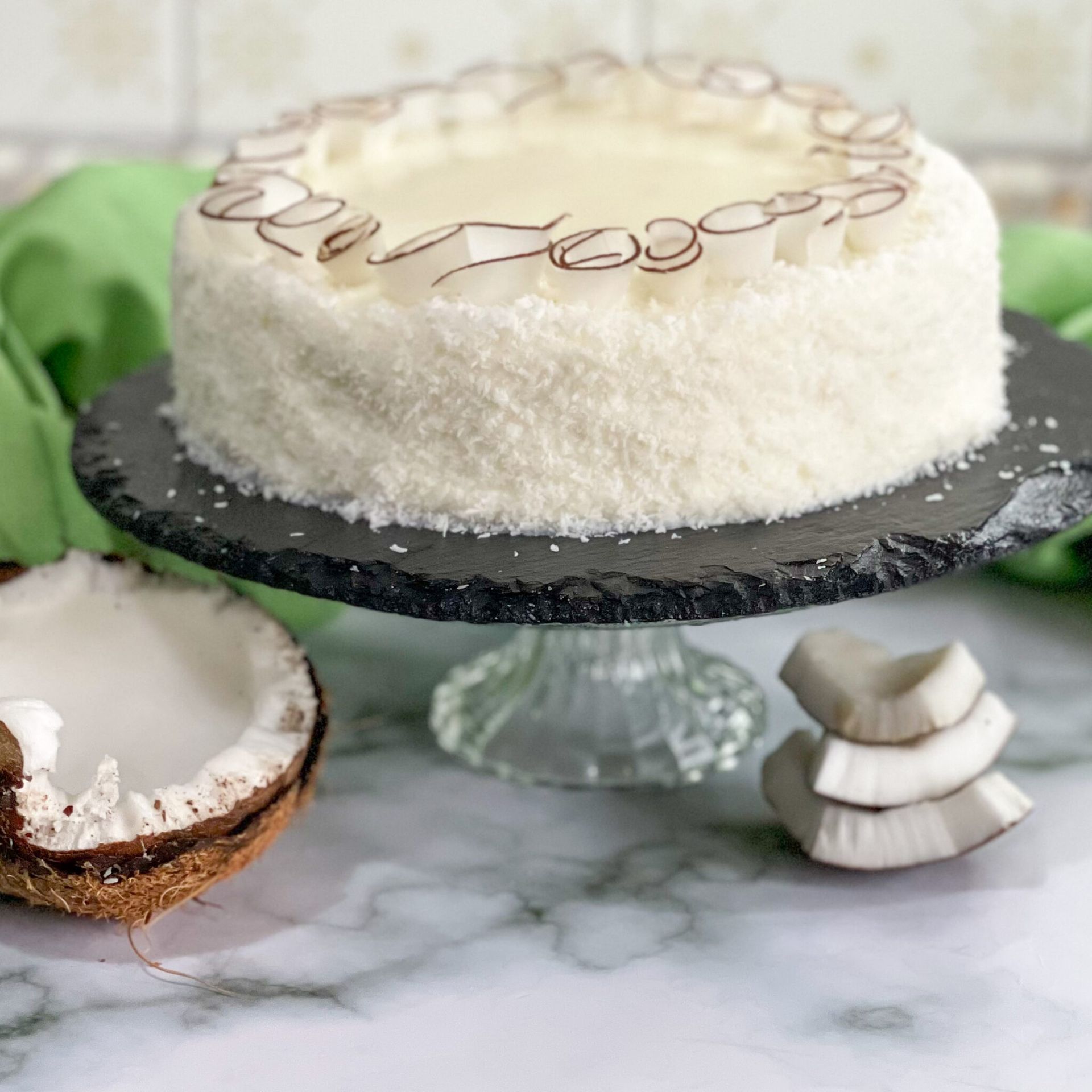 Una torta bianca è appoggiata su un'alzata per torte accanto a una noce di cocco.