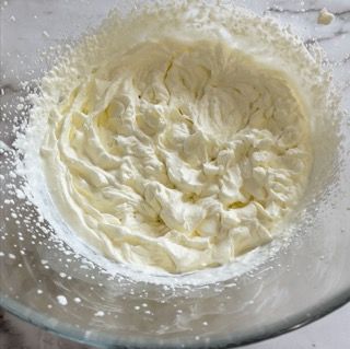 Una ciotola di vetro piena di panna montata su un tavolo.