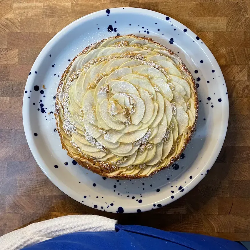 Torta di mele soffice e alta appena sfornata, con una superficie dorata di mele disposte a raggiera.