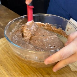 Una persona sta mescolando una ciotola di glassa al cioccolato con una spatola.