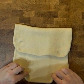 Una persona tiene in mano un pezzo di pasta su un tavolo di legno.