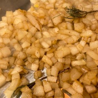 Una padella piena di patate tritate e un rametto di rosmarino