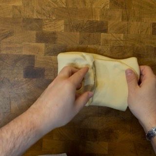 Una persona sta piegando un pezzo di pasta su un tavolo di legno.