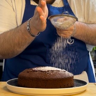Un uomo sta cospargendo di zucchero a velo una torta al cioccolato