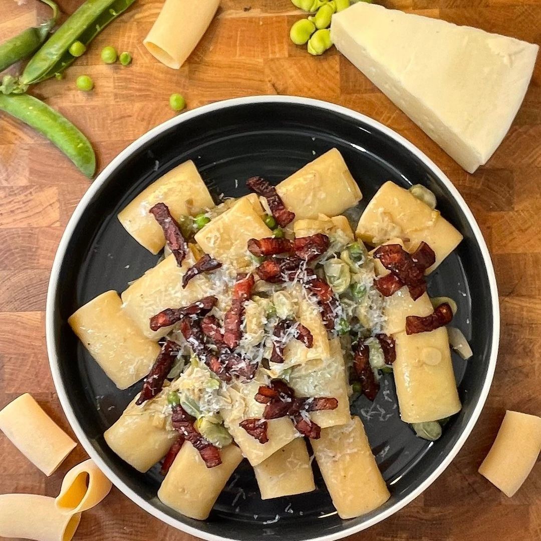 Una ciotola di pasta con pancetta e piselli su un tavolo di legno.