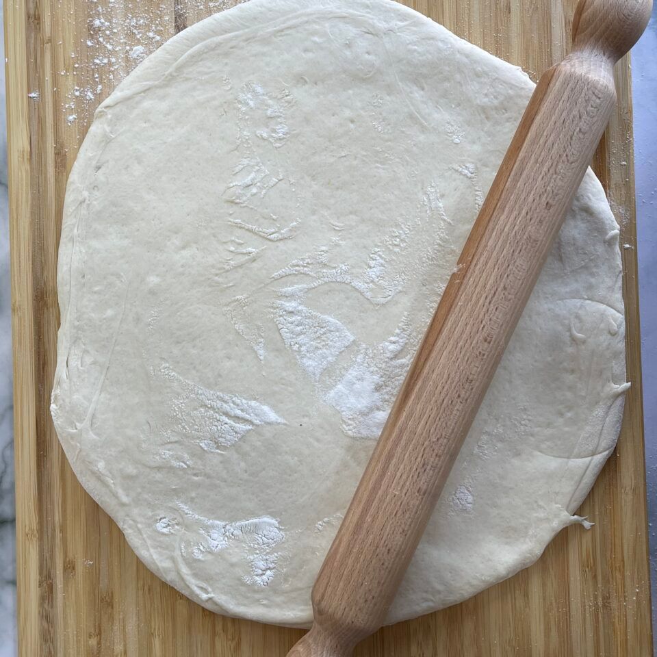 Un mattarello è appoggiato su un impasto per pizza su un tagliere.