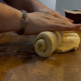 Una persona sta stendendo la pasta su un tavolo di legno