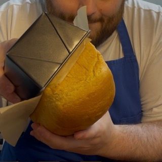 Un uomo con un grembiule tiene in mano una pagnotta