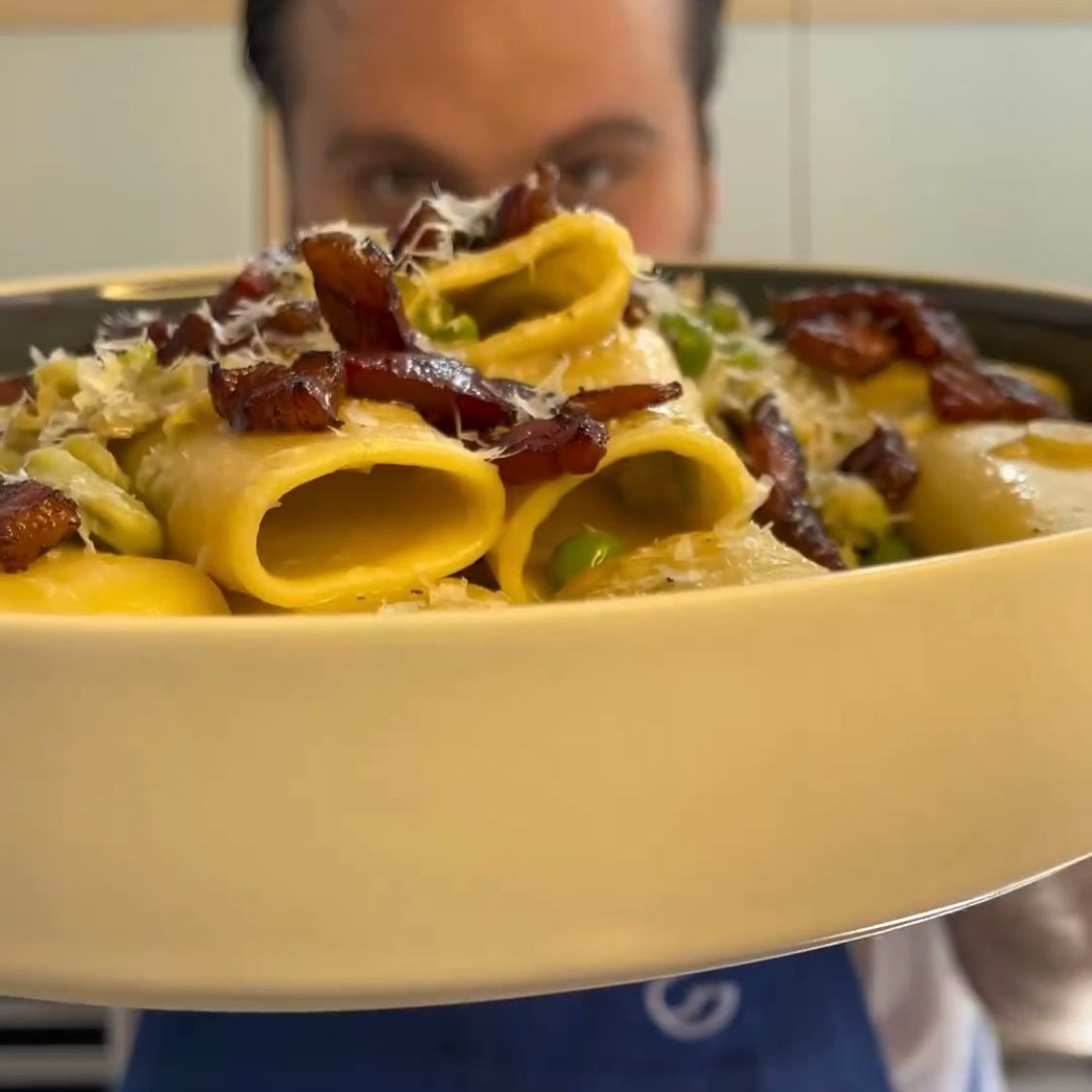 Un uomo tiene davanti al viso una ciotola di pasta con le verdure.