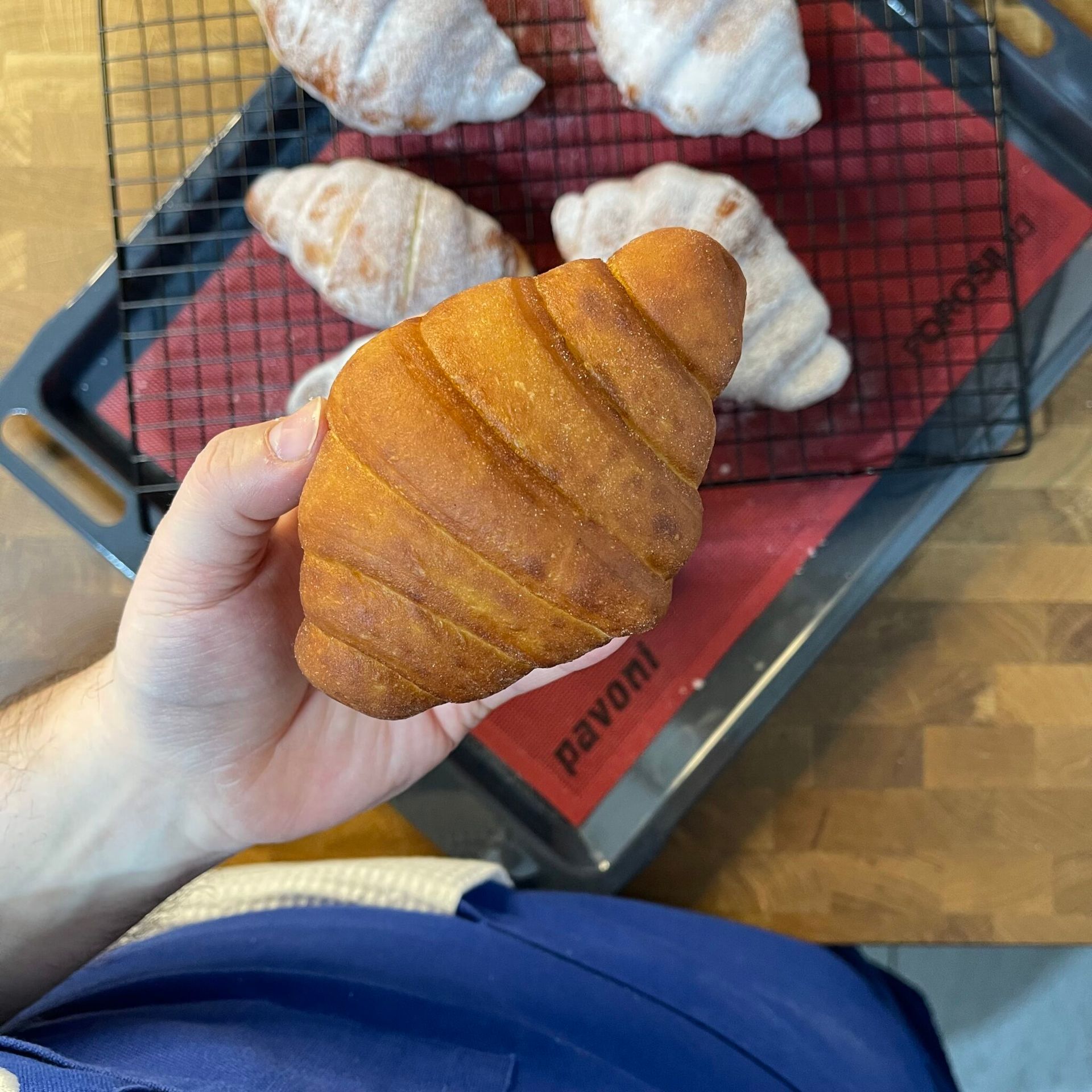 Una persona tiene in mano un croissant davanti a un tappetino pavoni